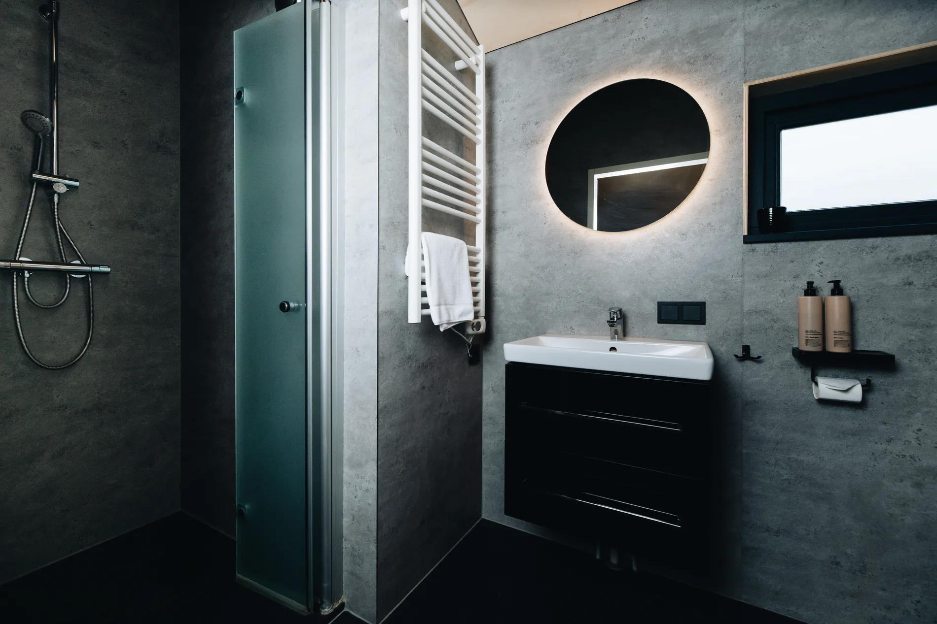 Moderne badkamer met industriële betonlook wanden en een ronde verlichte spiegel.